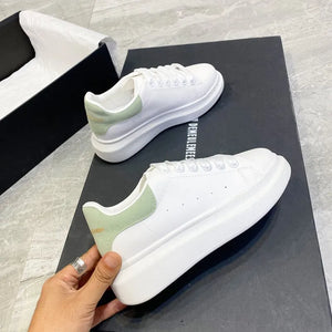 White platform sneakers with light green suede heel detail and white laces.