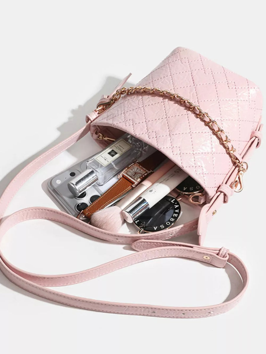 Pink quilted bucket bag with chain accent and leather strap, filled with makeup and accessories.