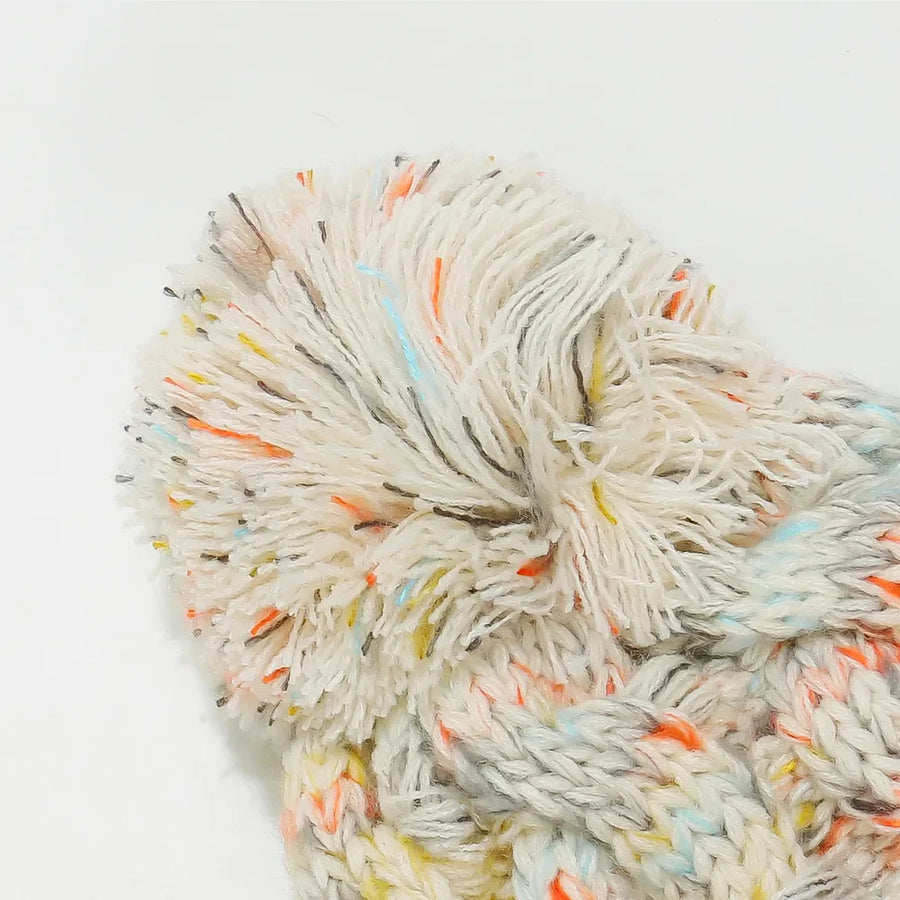 Textured knit pom beanie with colorful flecks and cable detail.