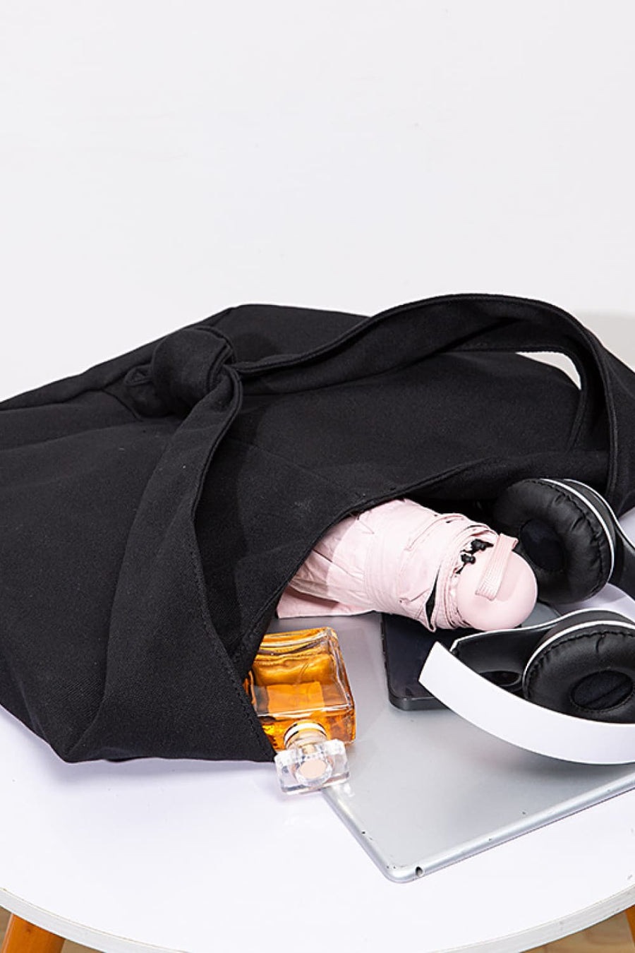 Black canvas shoulder bag with knotted strap detail, holding a perfume bottle and umbrella.