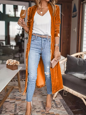 Tangerine velvet duster coat with fluid silhouette, open front, long sleeves, worn with jeans and heels.