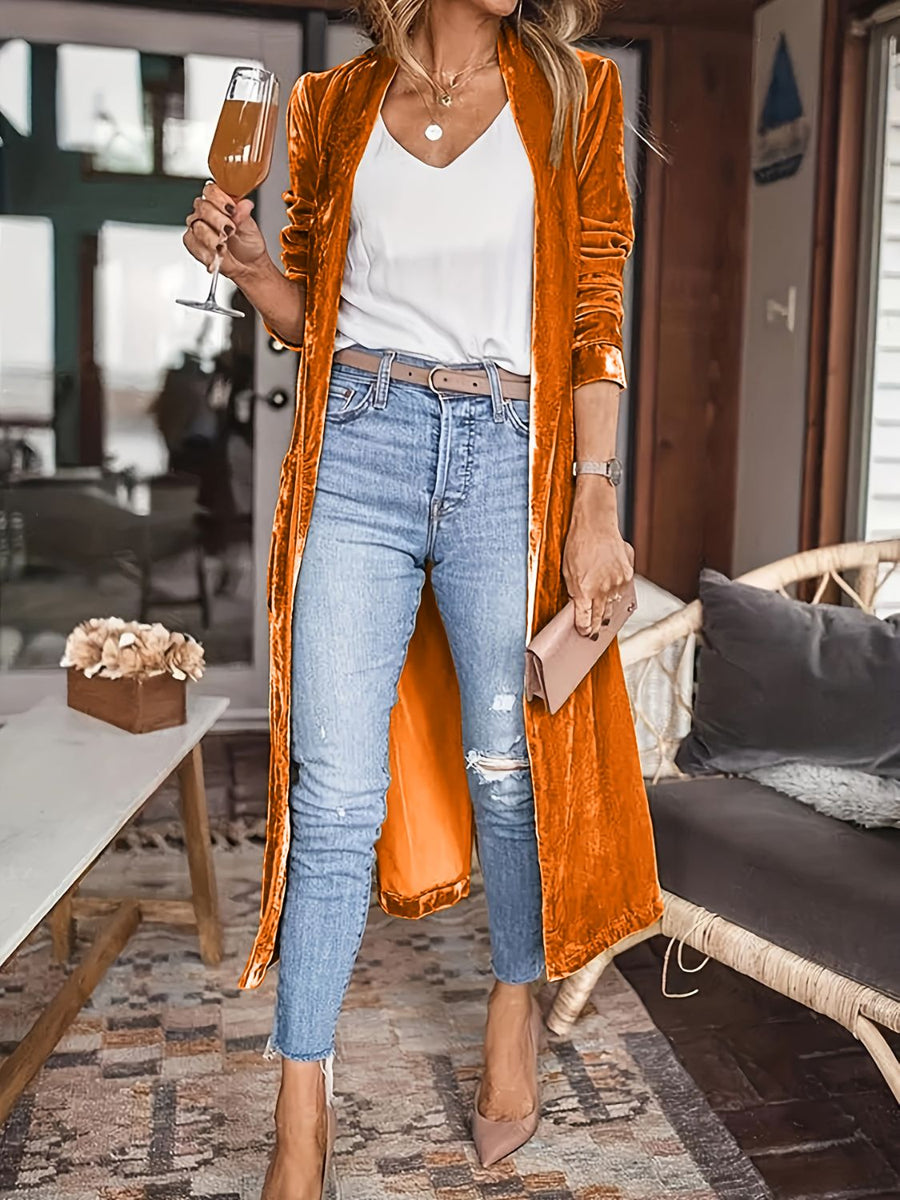 Tangerine velvet duster coat with fluid silhouette, open front, long sleeves, worn with jeans and heels.