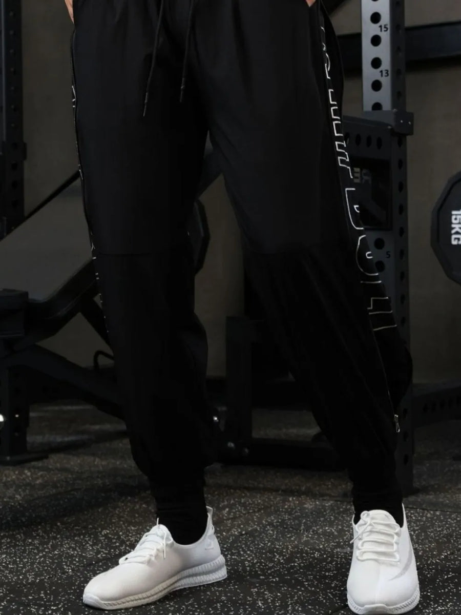 Black track pants with zip detail and white side graphic, worn with white sneakers.