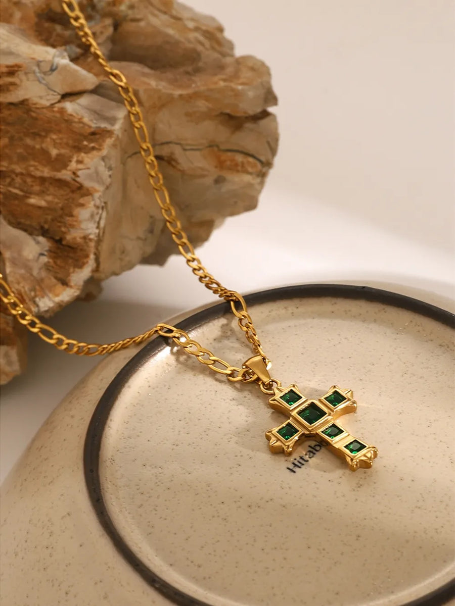 Gold cross pendant necklace with green zirconia stones on a figaro chain.