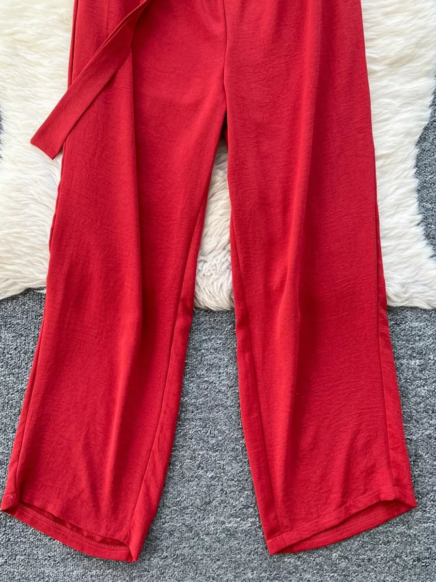 Red belted wide leg romper with textured fabric and tie waist detail.