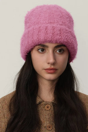 Textured bouclé knit beanie in hot pink, styled with a brown herringbone jacket.