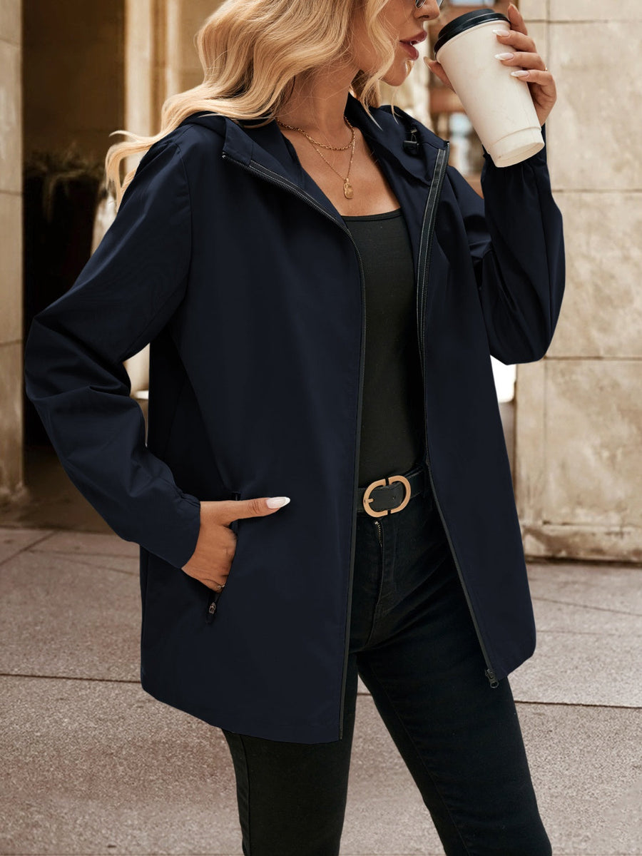 Navy zip-through hooded jacket with pockets, worn by a woman holding a coffee cup.
