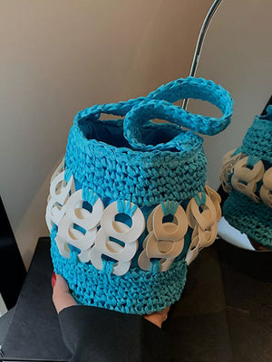 Blue woven straw bucket tote with white ring embellishments and braided handle.