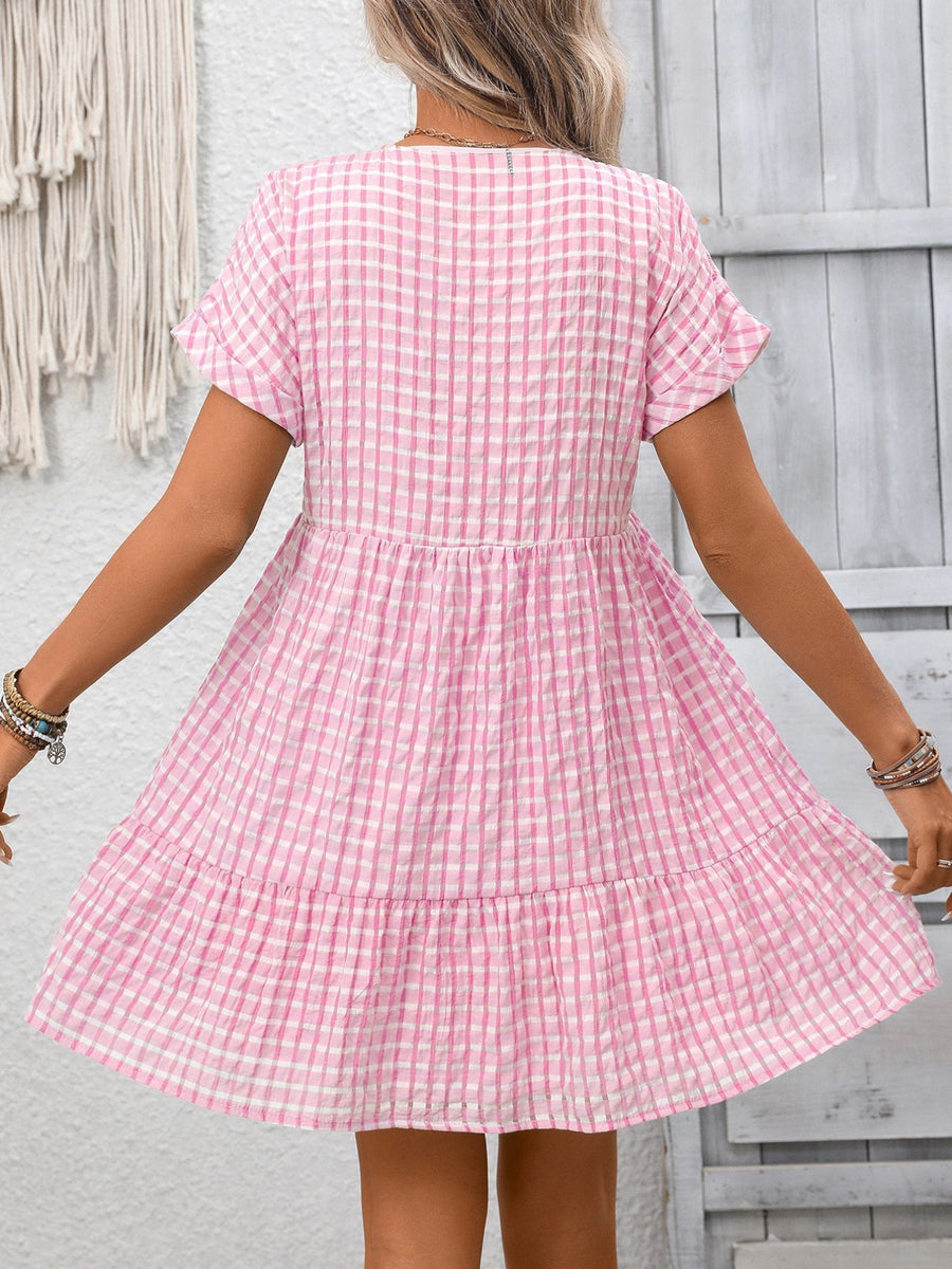 Pink plaid v-neck mini dress with short sleeves and tiered skirt.