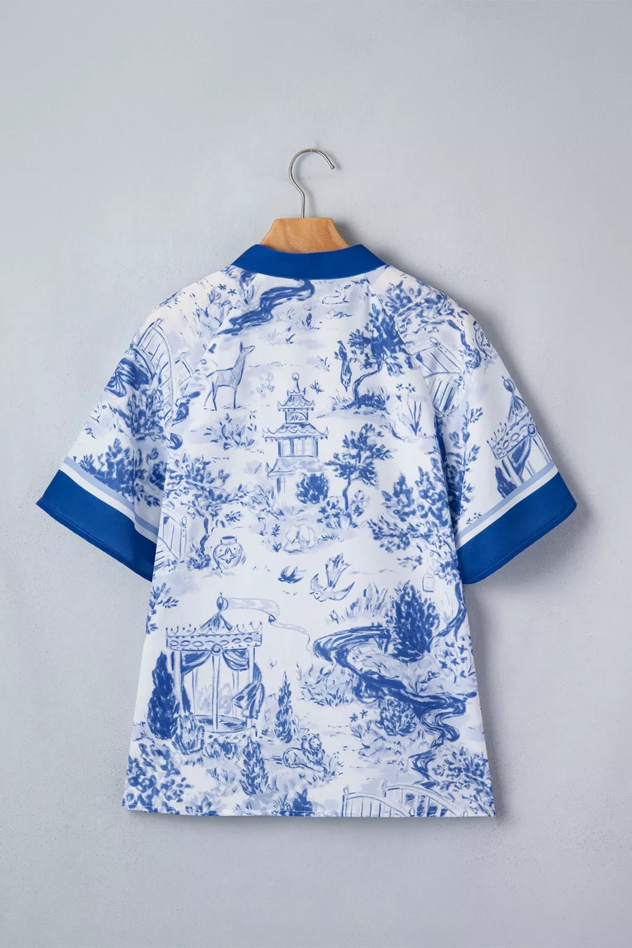 White polyester shirt with blue toile print, V-neck, short sleeves, and blue trim.