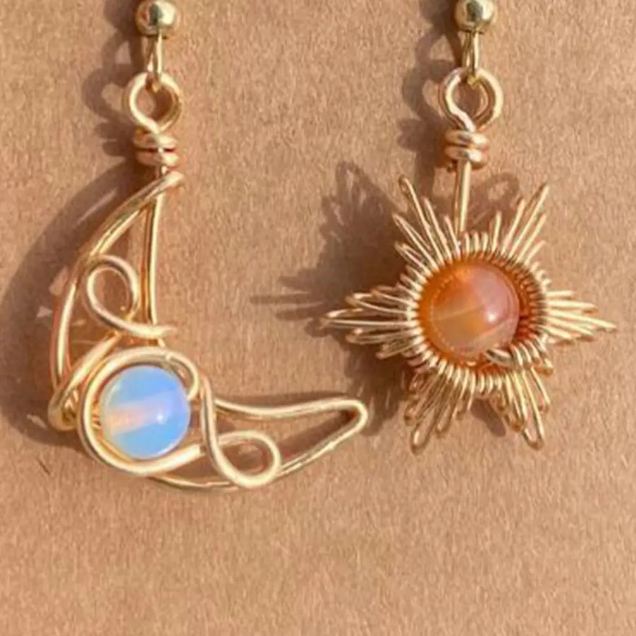 Gold celestial asymmetrical drop earrings with moon and sun charms and gemstone accents.