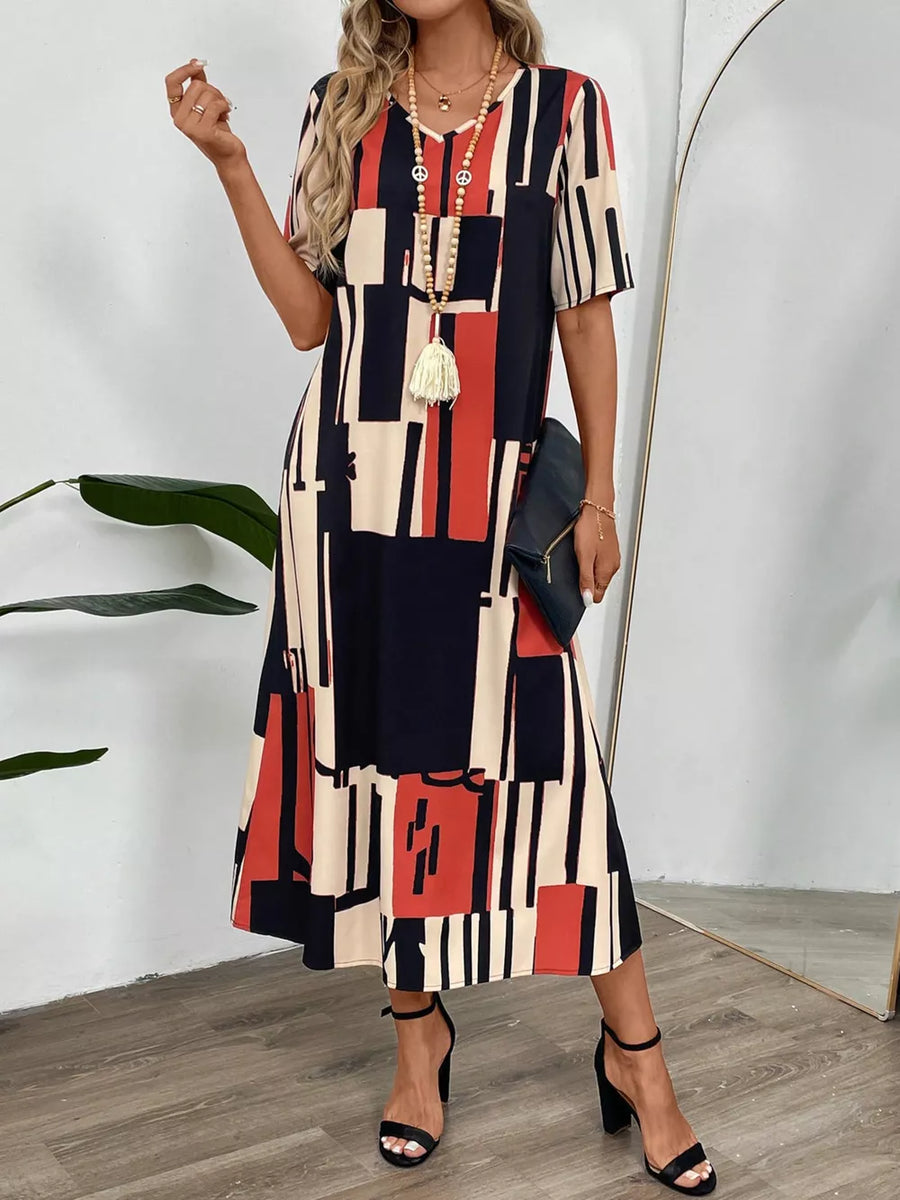 Geometric V-neck midi dress in dark blue, red, and cream with short sleeves and a flowing skirt.