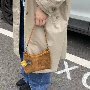 Brown suede crossbody bag with pom-pom charms and adjustable strap
