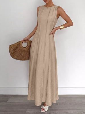 Textured beige maxi dress with elegant silhouette, sleeveless, round neck, and subtle pleating.