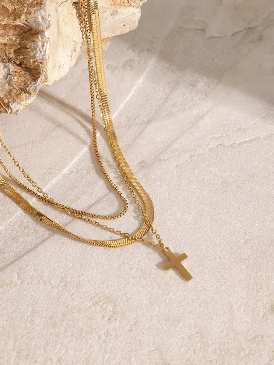 Gold layered necklace with herringbone and snake chains, featuring a small cross pendant.