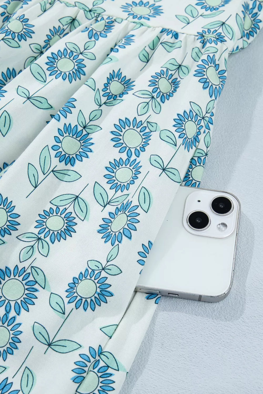 Floral print cotton blend dress in pastel blue with cap sleeves and a notched neckline, showing a side pocket.