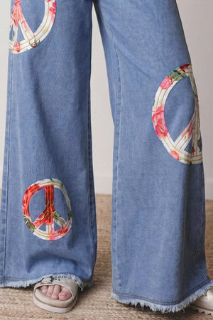 Light wash denim wide-leg jeans with floral peace sign appliqués and frayed hems.