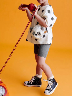Charming panda plush crossbody bag on a child wearing a black polka dot tee and grey biker shorts.