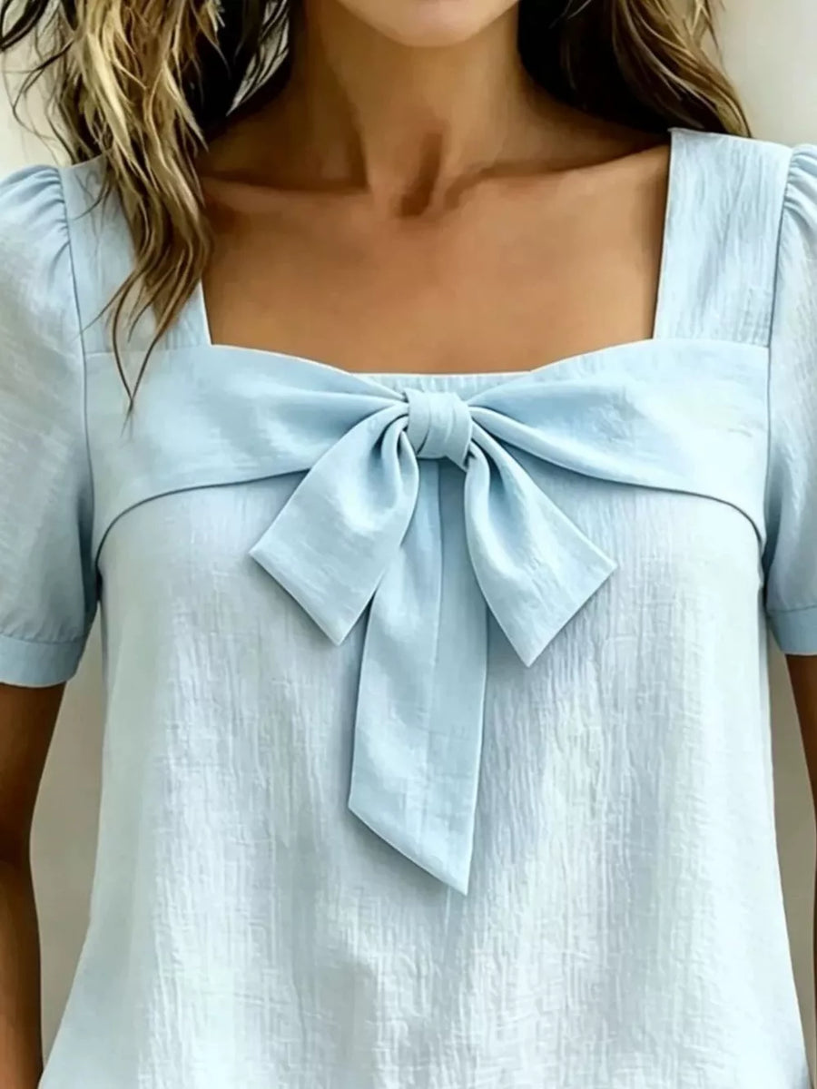 Sky blue puff sleeve shirt with a large bow tie detail and square neckline.