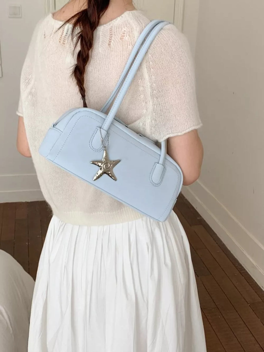 Light blue shoulder bag with star charm detail, worn by a woman in a white sweater.