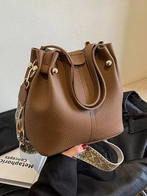 Brown textured crossbody bag with a unique patterned strap and gold hardware.