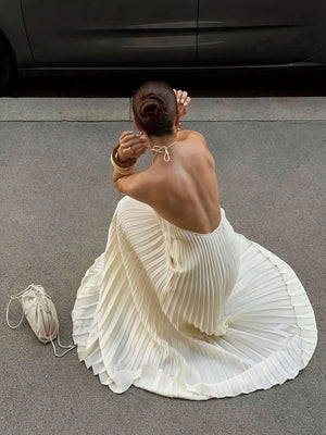 Backless pleated maxi dress in apricot with a halter neckline and flowing skirt.