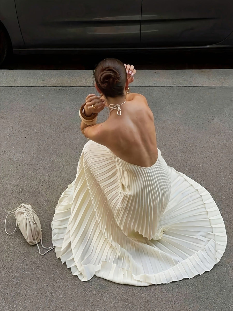 Backless pleated maxi dress in apricot with a halter neckline and flowing skirt.