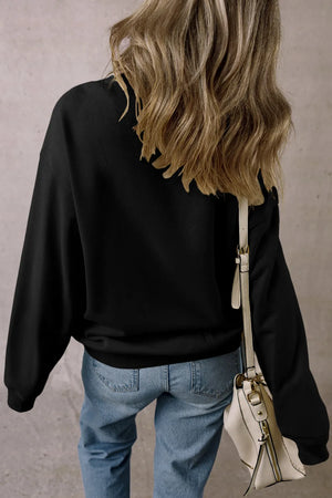Black crewneck sweatshirt with long sleeves, casual fit, worn with jeans and a cream crossbody bag.