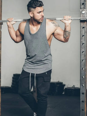 Scoop neck muscle tank top in dark gray with a relaxed fit, worn by a man in a gym.