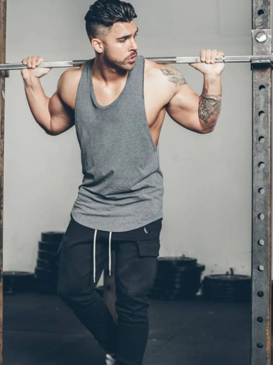 Scoop neck muscle tank top in dark gray with a relaxed fit, worn by a man in a gym.