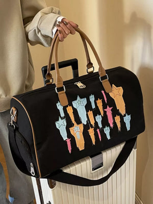 Black canvas duffle bag with colorful star design and tan leather handles.