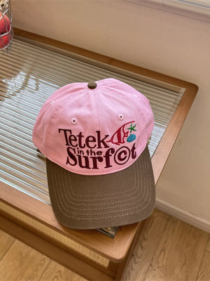 Pink cotton baseball cap with brown brim and embroidered text.