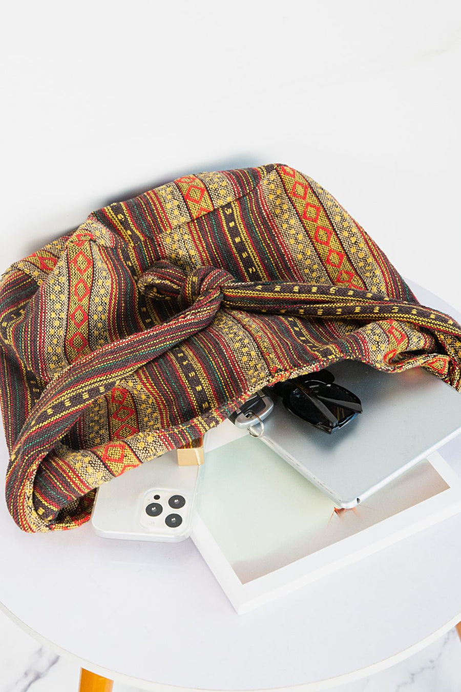 Tribal weave shoulder bag in multicolor canvas with knotted strap detail, holding a phone and sunglasses.