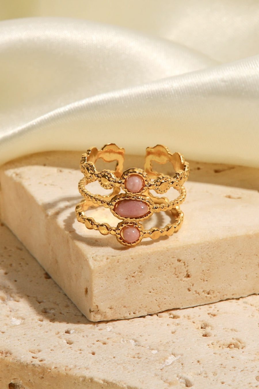 Gold triple stone openwork ring with pink stones and textured bands.