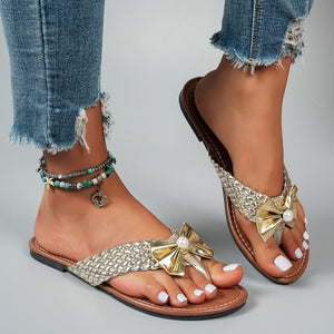 Gold bow embellished flat sandals with woven straps and pearl detail.