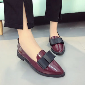 Patent leather loafers in burgundy with black bow detail.
