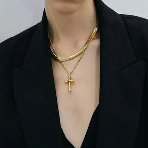 Gold cross pendant necklace layered with a herringbone chain necklace.
