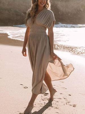 Elegant V-neck maxi dress in Apricot with dolman sleeves and smocked waist, flowing on a beach.