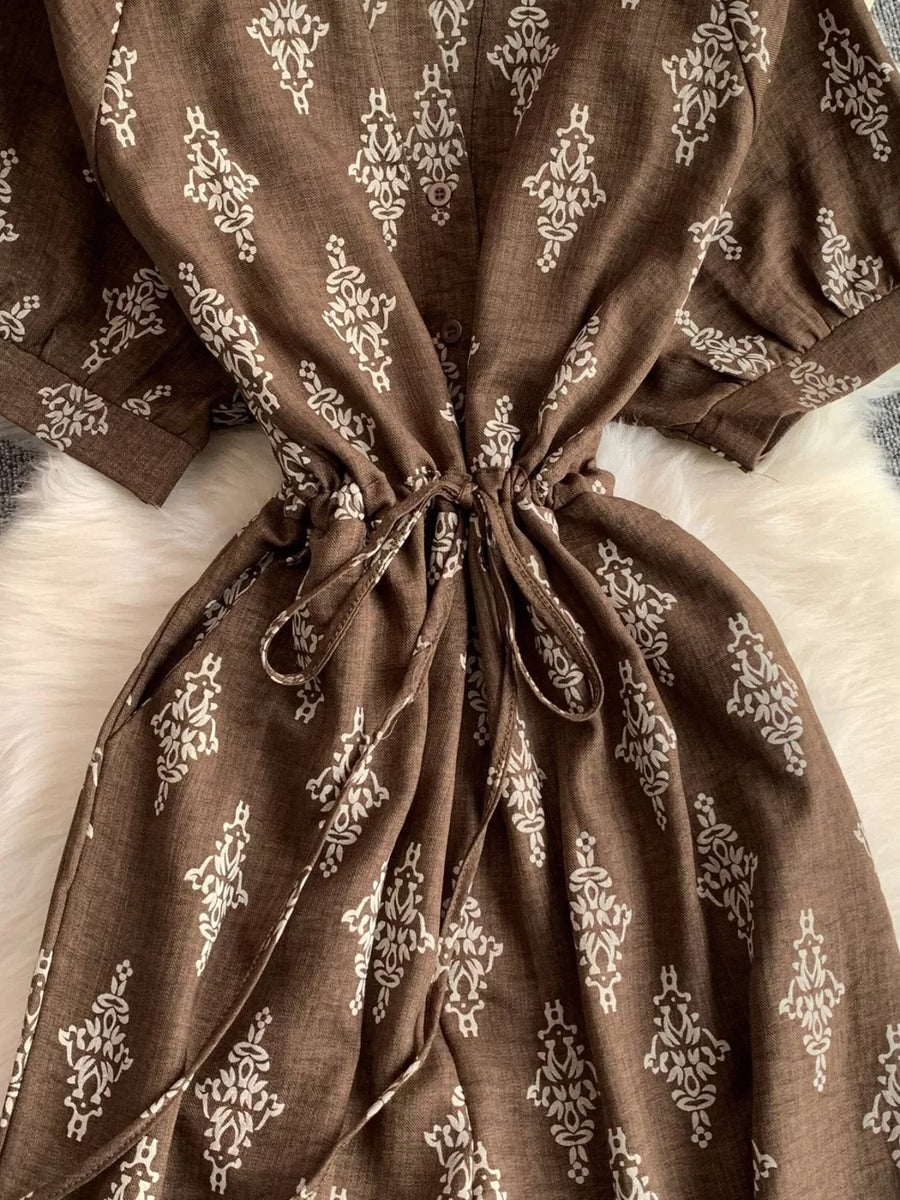 Brown drawstring jumpsuit with white pattern, short sleeves, and cinched waist.