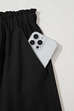 Black cropped drawstring pants with elastic waist and pocket holding a smartphone.