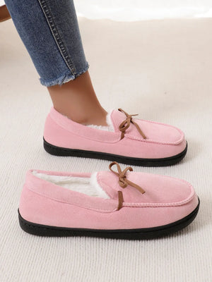 Pink suede moccasin slippers with faux fur lining and bow detail.