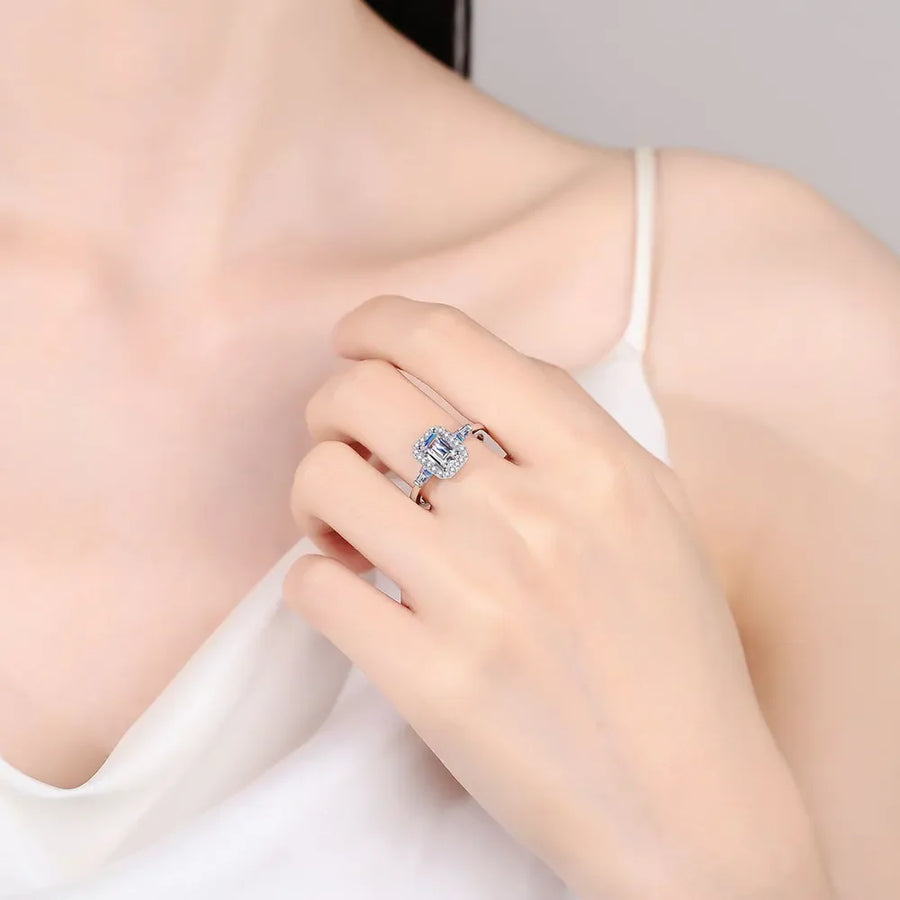 Emerald cut moissanite halo ring in sterling silver with blue accents.