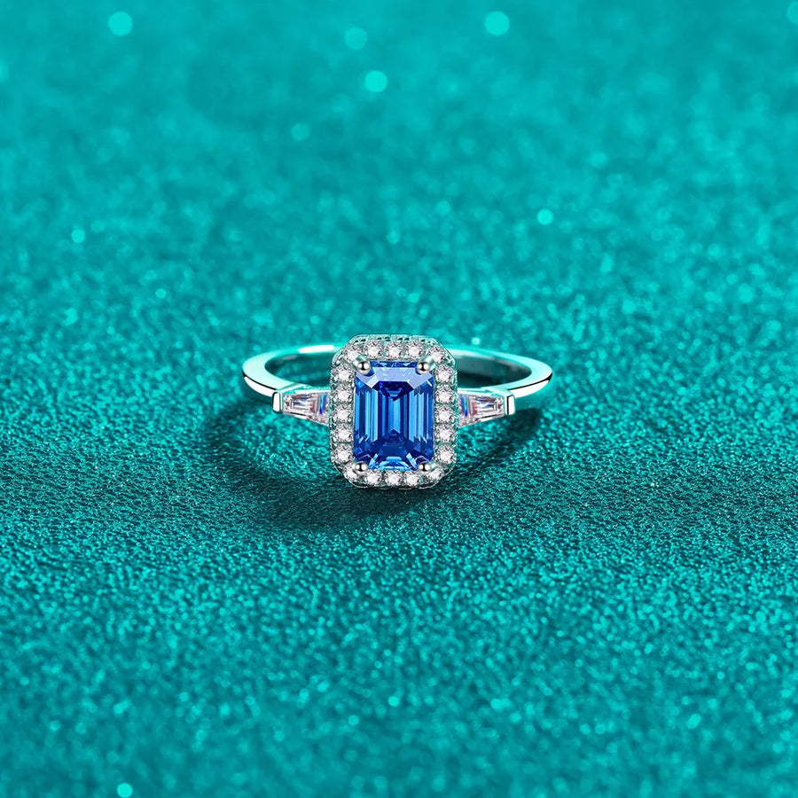 Royal blue emerald cut moissanite halo ring in sterling silver with baguette accents.