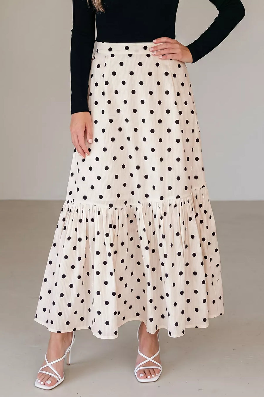 Beige polka dot maxi skirt with ruffled hem, styled with white strappy heels.