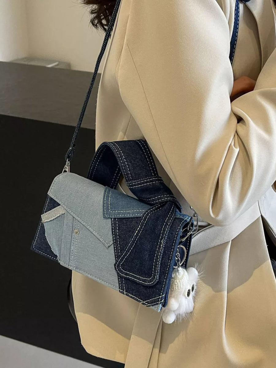 Artisanal patchwork denim crossbody bag in light blue and dark blue with white stitching and a fluffy charm.