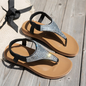 Sparkling rhinestone flat thong sandals with black elastic straps and tan soles.
