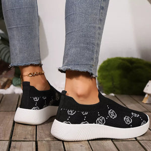 Black mesh slip-on sneakers with white geometric pattern and white soles.
