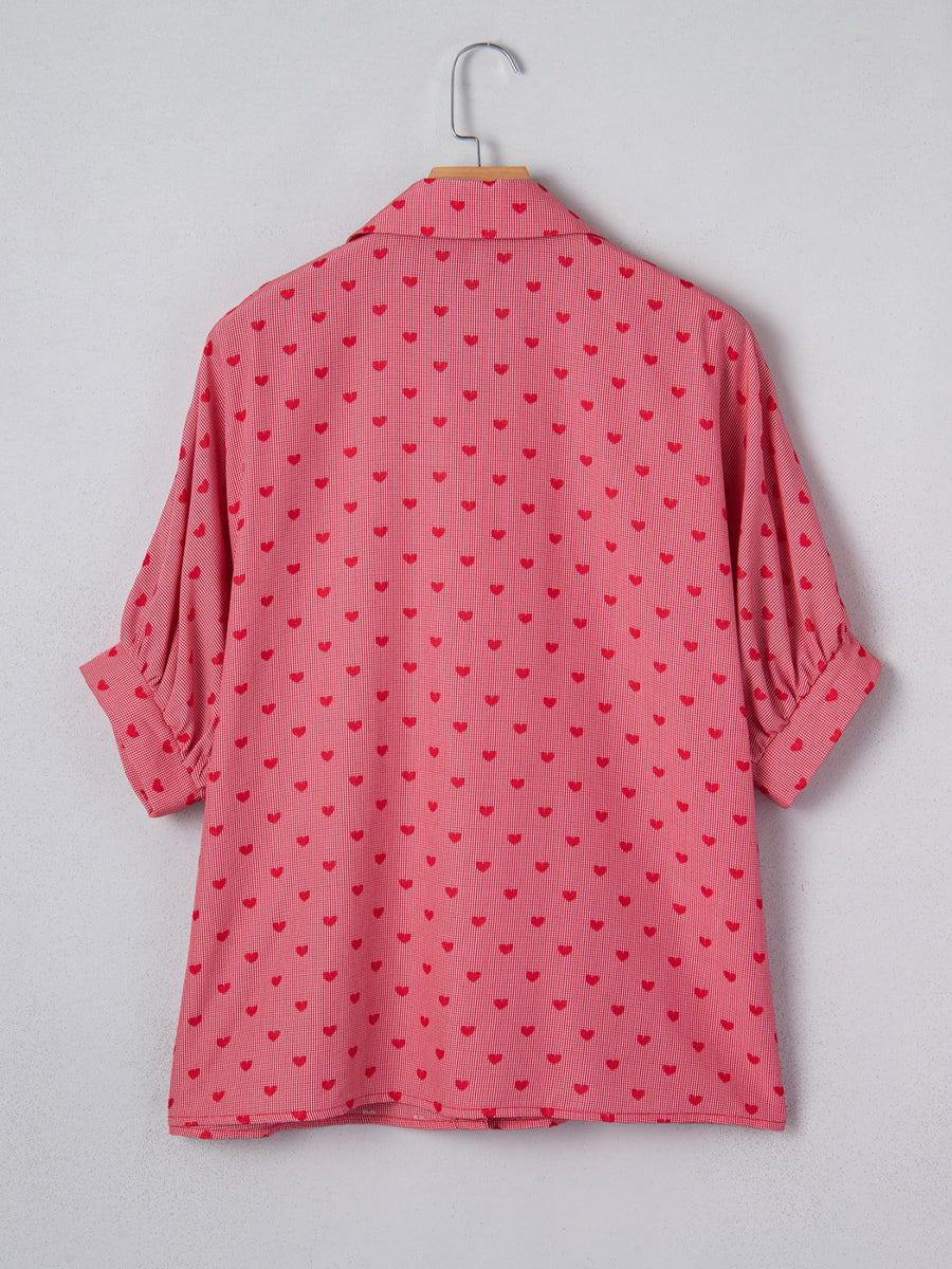 Pink button-down shirt with red hearts pattern, cuffed short sleeves, and classic collar.