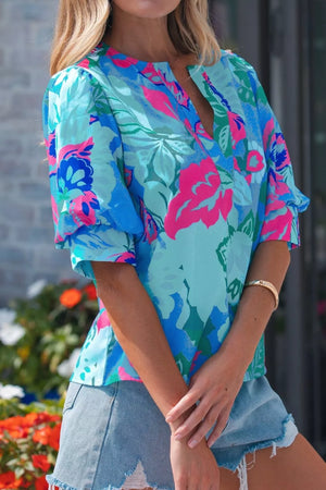 Vibrant floral V-neck blouse with relaxed fit and puff sleeves, styled with denim shorts.