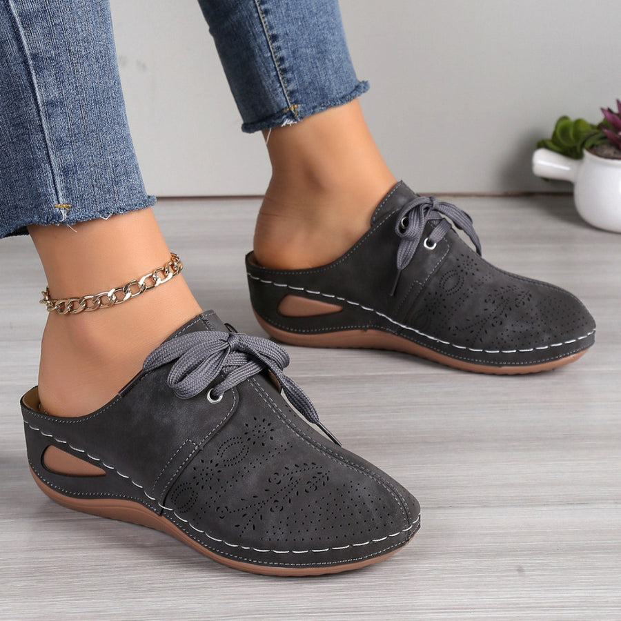 Dark gray perforated slip-on mules with lace-up detail and white stitching.
